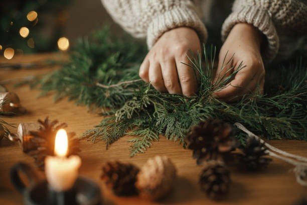 Hands arranging evergreen branches into a wreath by candlelight